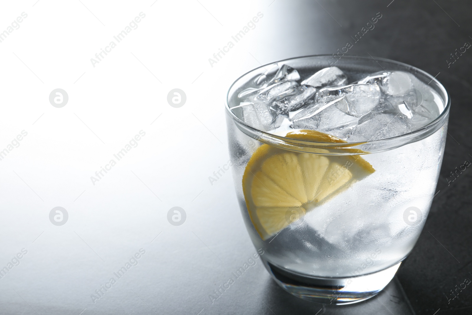 Photo of Water with ice cubes and lemon on grey table, closeup. Space for text