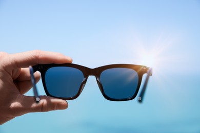 Mature man holding stylish sunglasses against blue sky, closeup