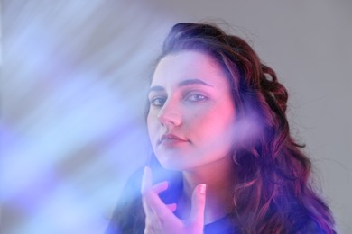 Fashionable portrait of beautiful young woman on grey background with colorful led lights, closeup