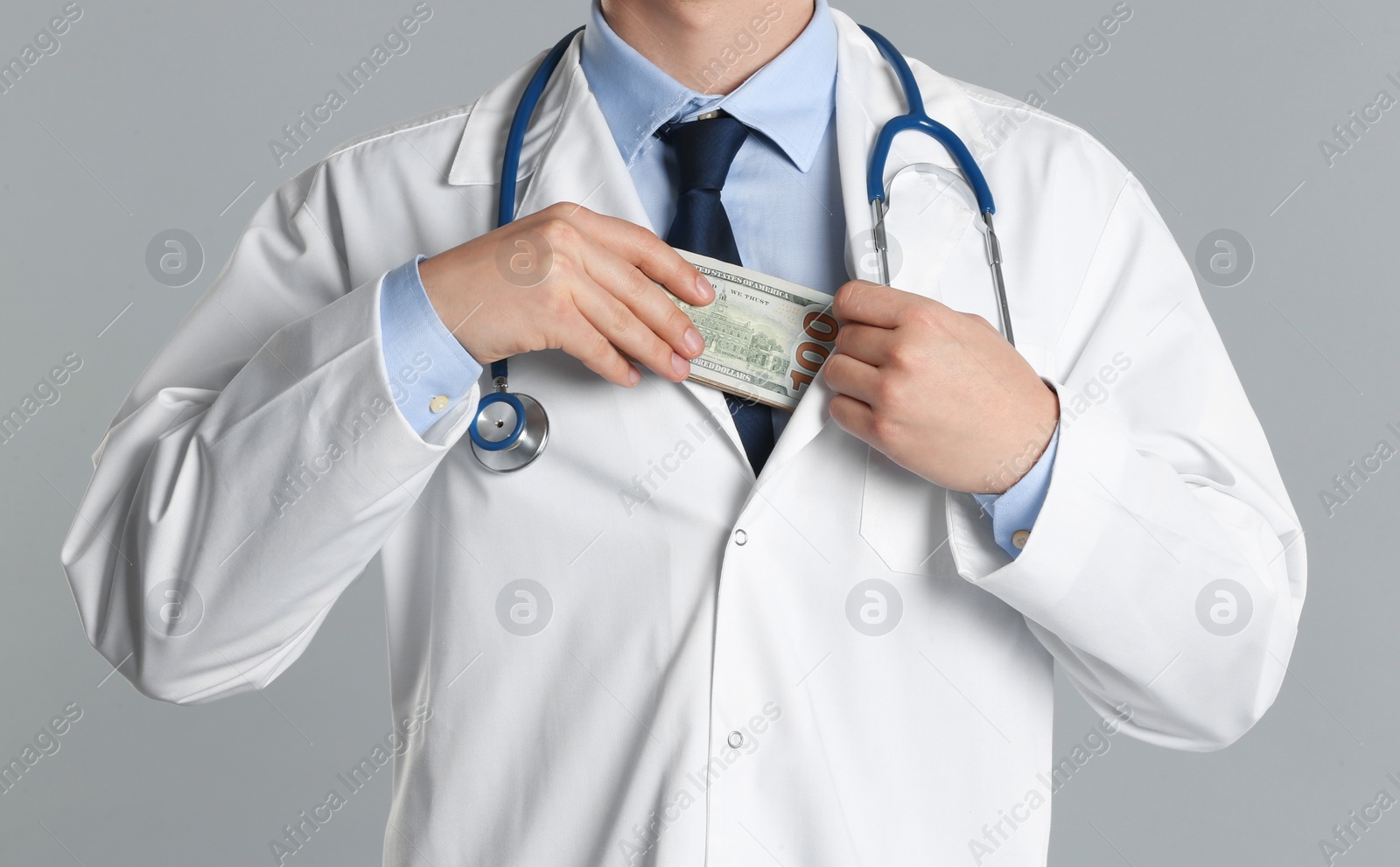 Photo of Doctor putting bribe into pocket on grey background, closeup. Corruption in medicine