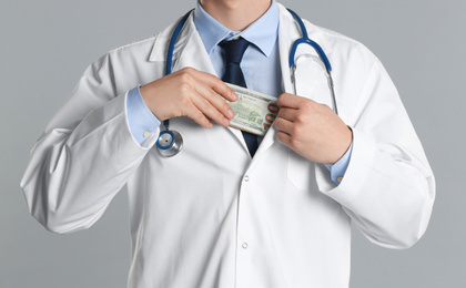 Doctor putting bribe into pocket on grey background, closeup. Corruption in medicine