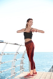 Young woman doing fitness exercises on pier in morning