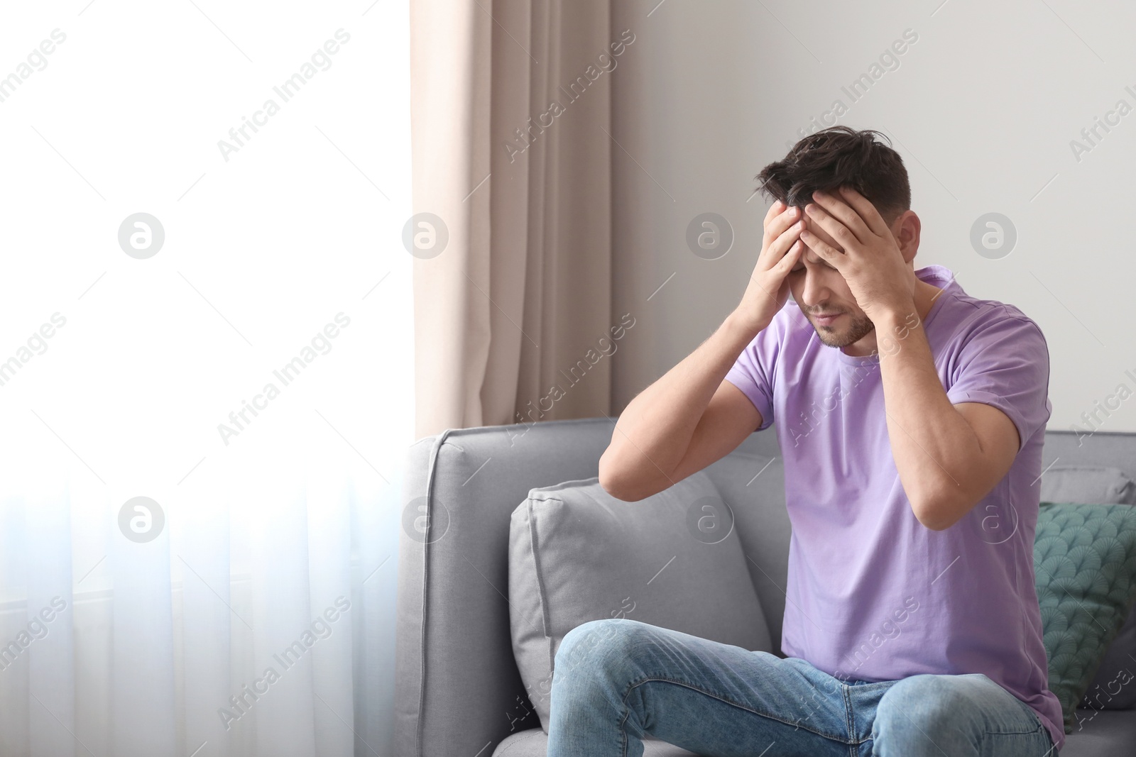 Photo of Young man suffering from headache at home