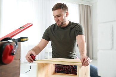 Photo of Young working man using measure tape at home