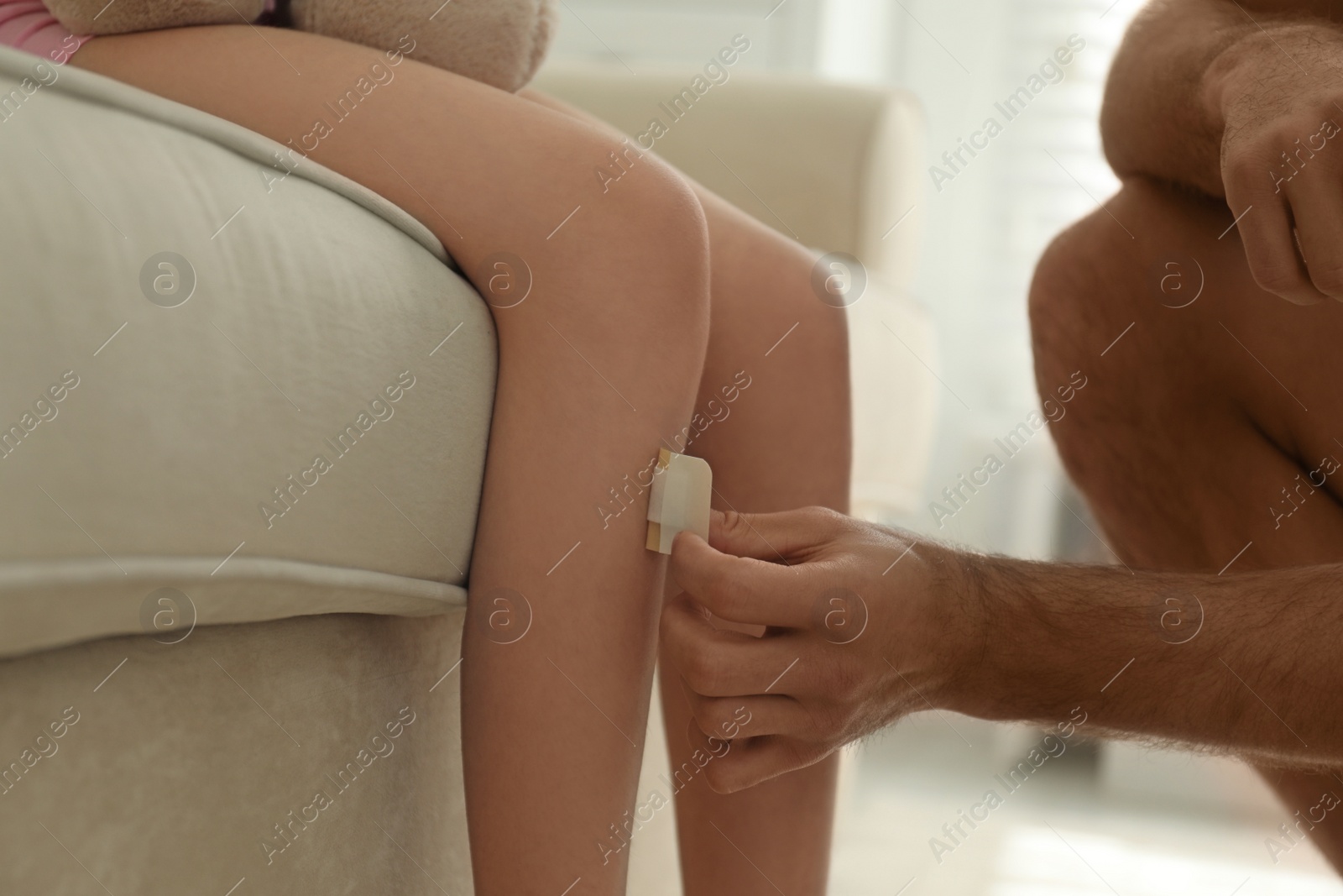 Photo of Father putting sticking plaster onto daughter's leg at home, closeup