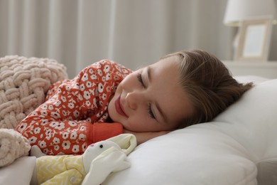 Photo of Cute little girl with toy bunny sleeping in bed at home