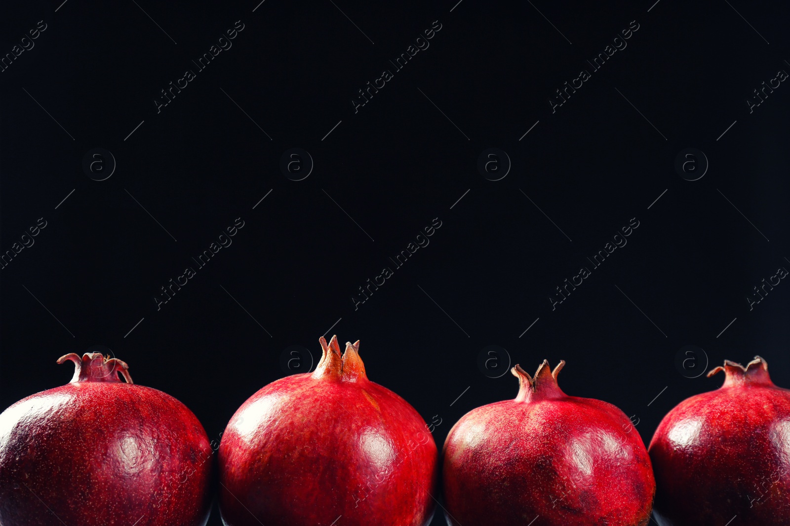 Photo of Ripe pomegranates on black background, space for text