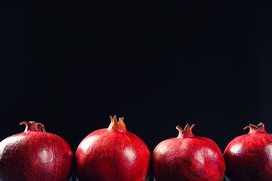 Ripe pomegranates on black background, space for text