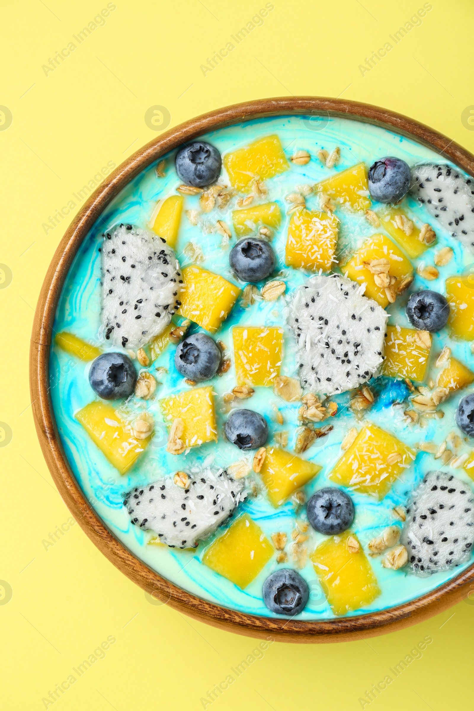 Photo of Delicious smoothie bowl with fresh fruits, blueberries and oatmeal on yellow background, top view