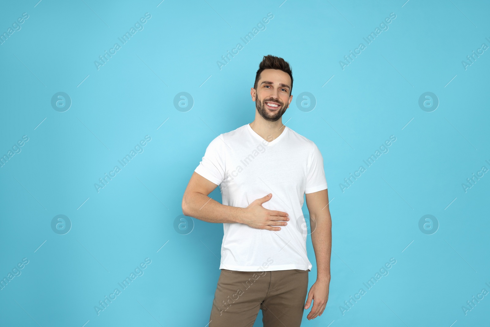Photo of Happy man touching his belly on light blue background. Concept of healthy stomach