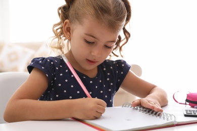 Photo of Cute little girl doing homework at table