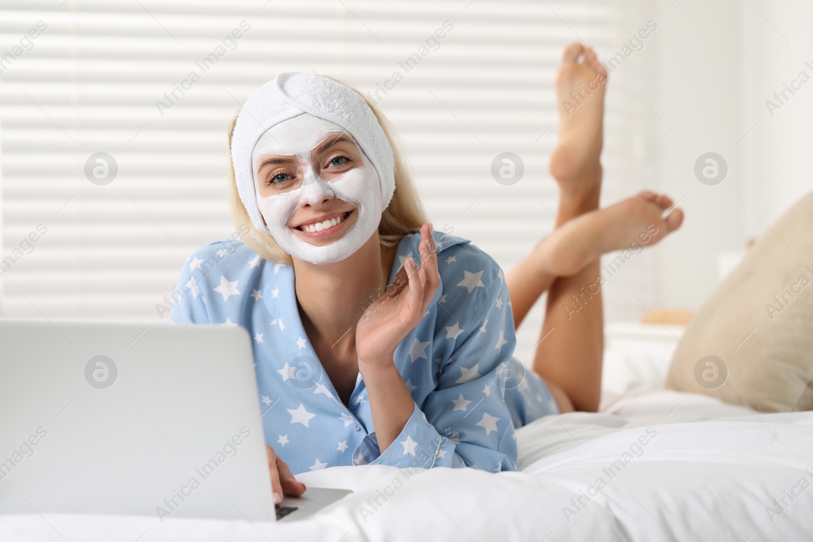 Photo of Young woman with face mask using laptop on bed at home. Spa treatments