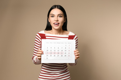 Photo of Young woman holding calendar with marked menstrual cycle days on beige background