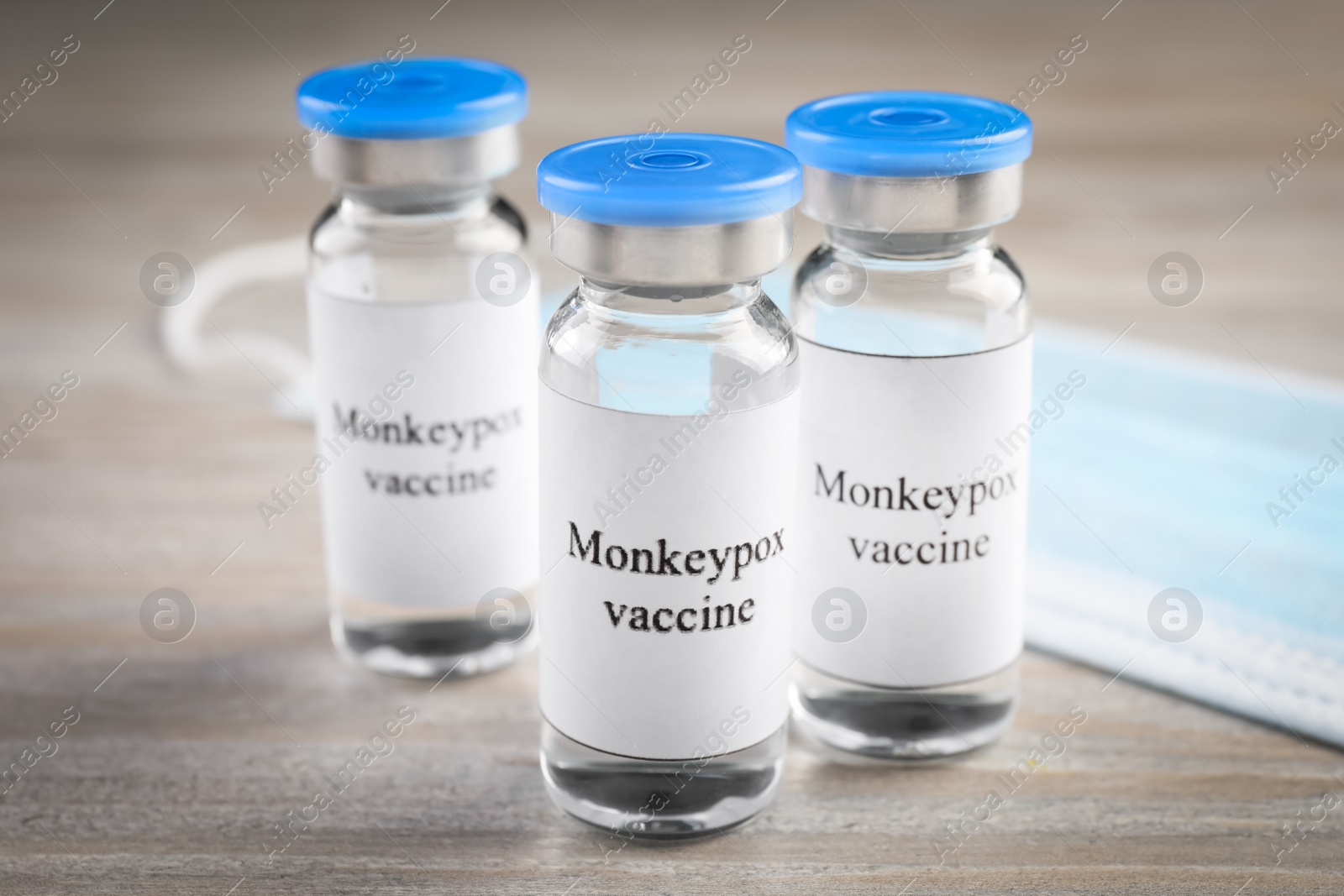 Photo of Monkeypox vaccine in glass vials and medical mask on wooden table
