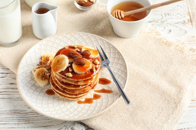 Stack of tasty pancakes with banana, nuts and syrup on table