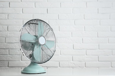 Photo of Electric fan on table near white brick wall, space for text. Summer heat