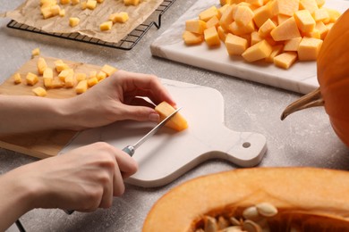 Photo of Woman cutting fresh pumpkin at light grey table, closeup