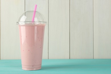 Photo of Tasty smoothie in plastic cup on light blue table against white wooden wall. Space for text