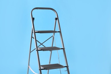 Photo of Metal stepladder on light blue background, space for text. Construction equipment