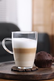 Photo of Cup of aromatic latte macchiato and chocolate muffin on table against blurred background