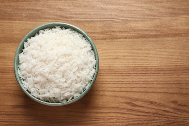 Photo of Bowl of tasty cooked rice on wooden background, top view. Space for text