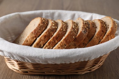 Photo of Fresh bread slices in wicker basket on wooden table, closeup