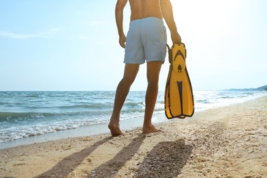 Back view of man with flippers walking on beach, closeup