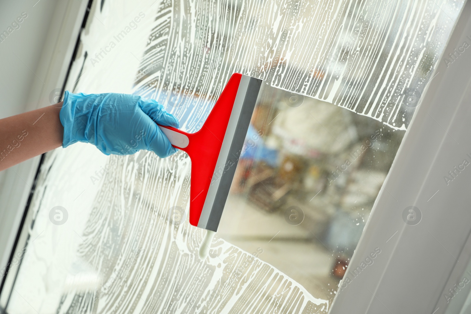 Photo of Woman cleaning window with squeegee indoors, closeup