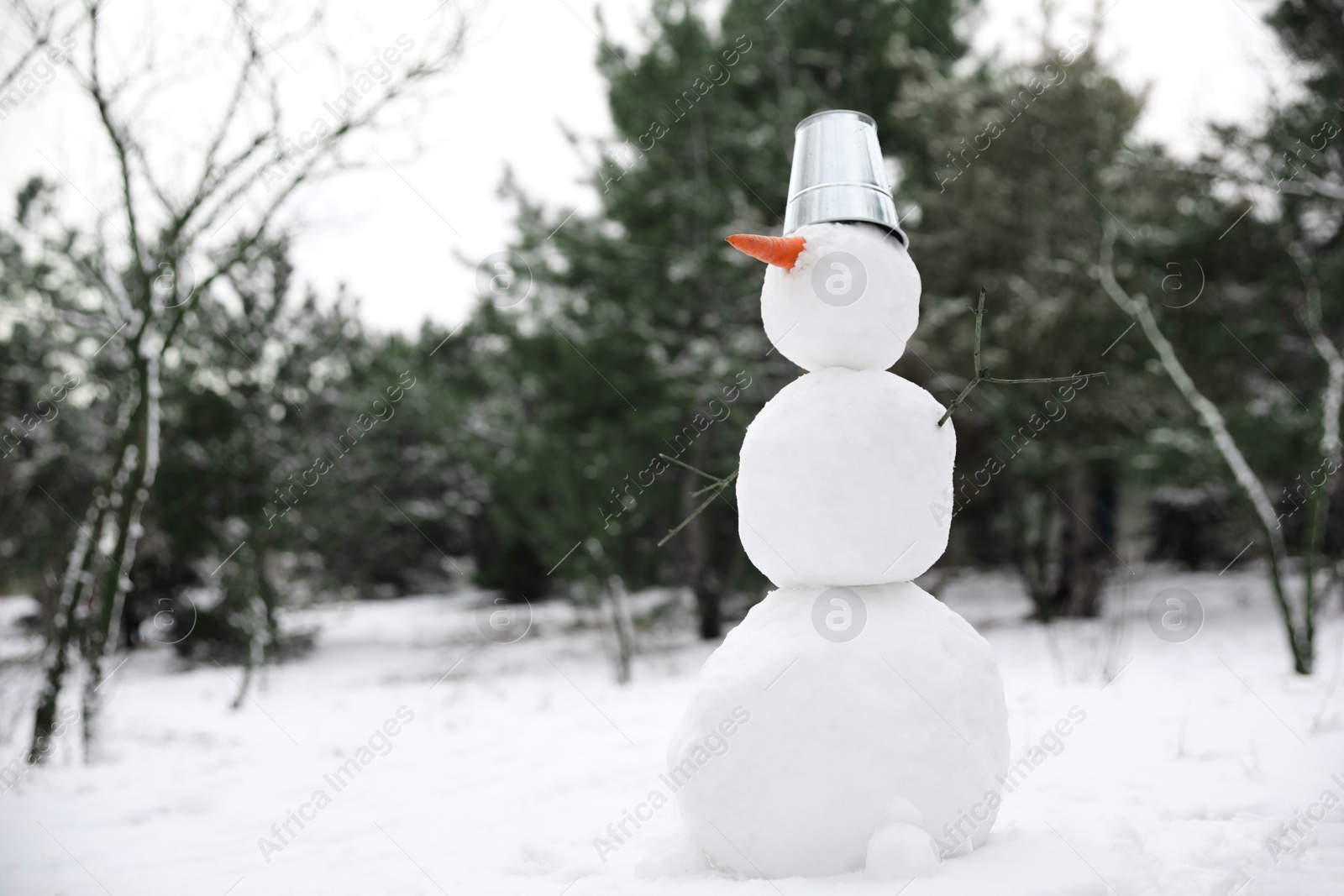 Photo of Cute snowman with metal bucket and carrot nose outdoors on winter day, space for text