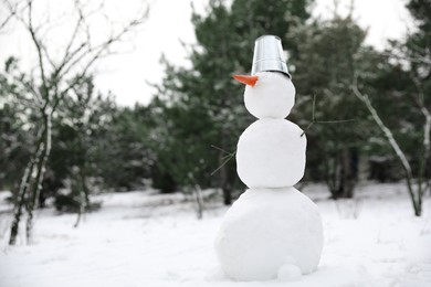 Photo of Cute snowman with metal bucket and carrot nose outdoors on winter day, space for text