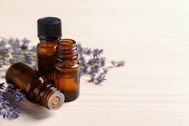 Photo of Essential oil and lavender flowers on white wooden table, space for text