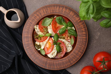 Photo of Plate of delicious Caprese salad with pesto sauce and ingredients on brown textured table, flat lay