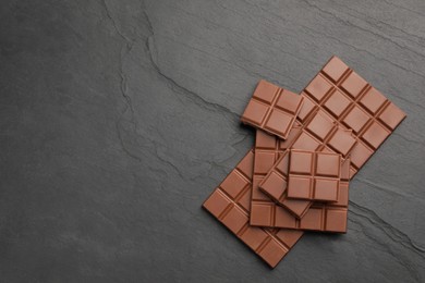 Photo of Delicious milk chocolate on black table, flat lay. Space for text