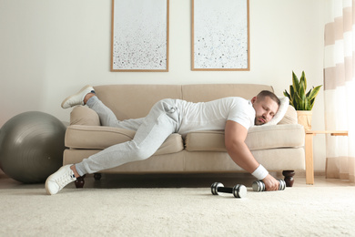 Photo of Lazy overweight man with dumbbells sleeping on sofa at home