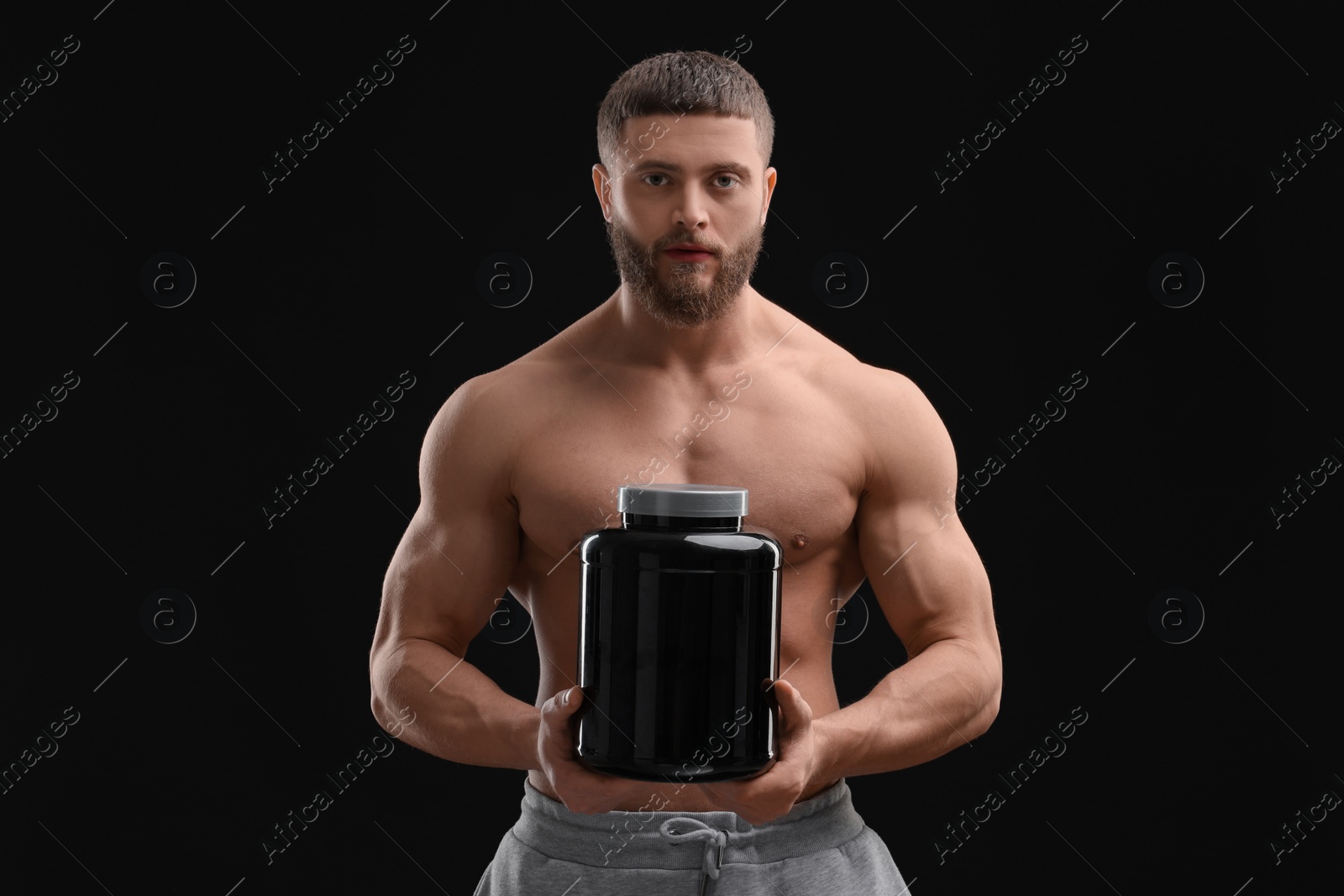 Photo of Young man with muscular body holding jar of protein powder on black background
