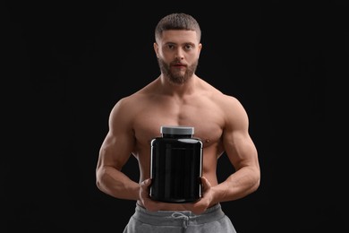 Young man with muscular body holding jar of protein powder on black background