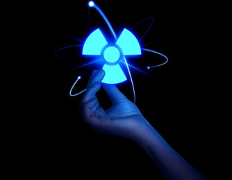Woman holding glowing atom symbol with radiation warning sign on black background, closeup