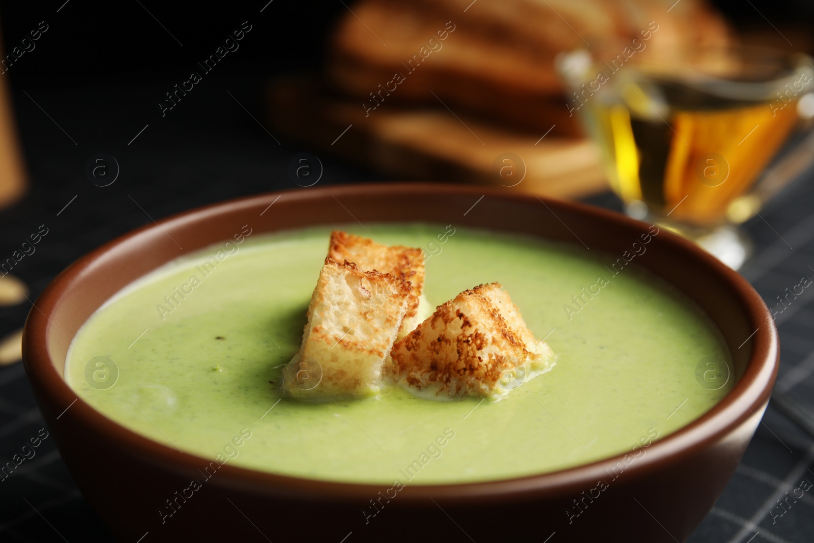 Photo of Bowl of delicious broccoli cream soup with croutons on table, closeup