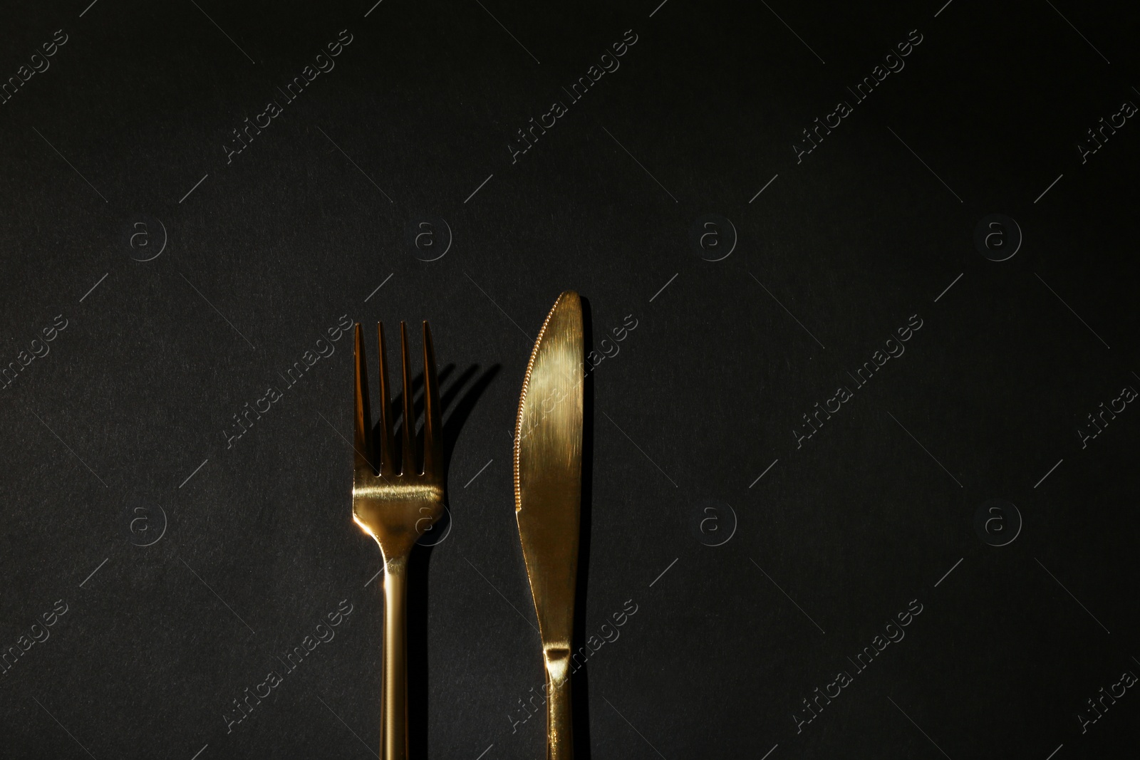 Photo of Gold fork and knife on black background, top view. Space for text