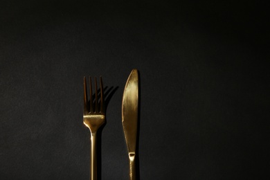 Photo of Gold fork and knife on black background, top view. Space for text