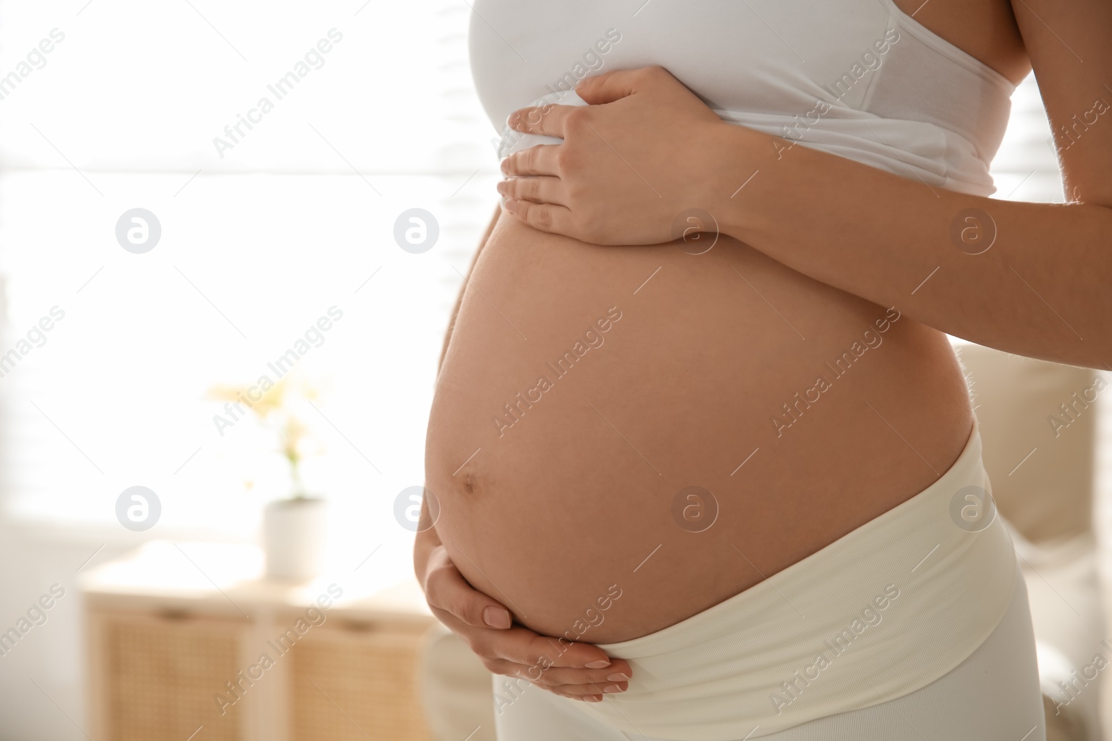 Photo of Pregnant woman touching her belly indoors, closeup