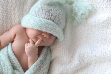 Photo of Cute newborn baby in warm hat lying on white plaid, top view. Space for text