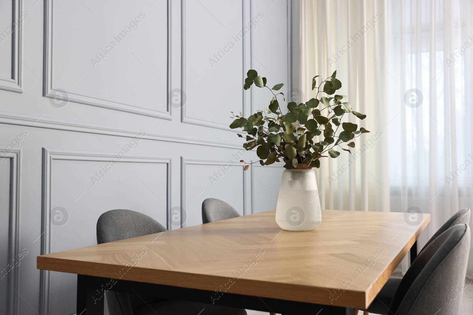 Photo of Vase with eucalyptus branches on wooden table in stylish dining room