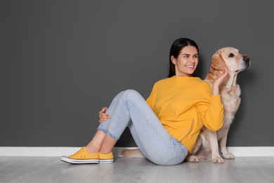 Photo of Happy woman with cute Labrador Retriever on floor against grey wall