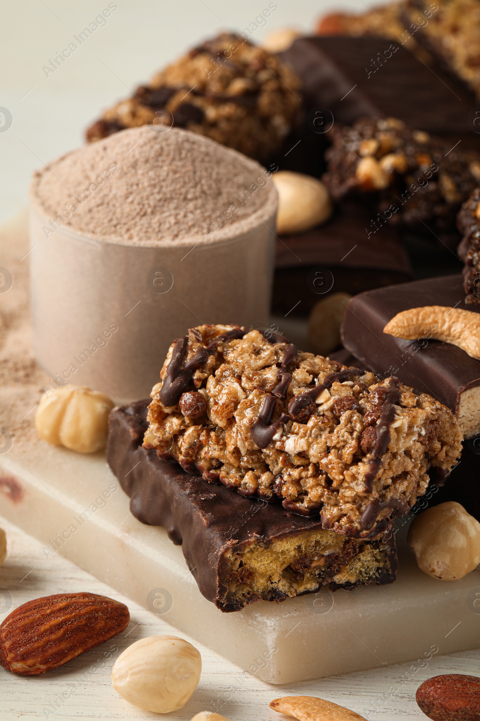 Photo of Different tasty energy bars, nuts and protein powder on white table, closeup