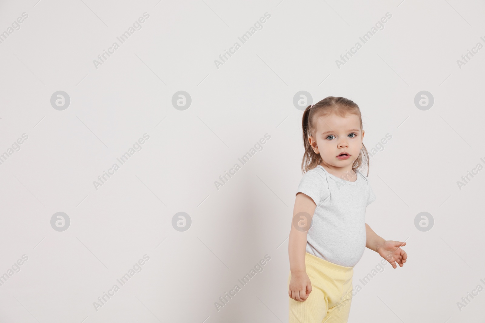Photo of Cute little girl standing near white wall at home, space for text