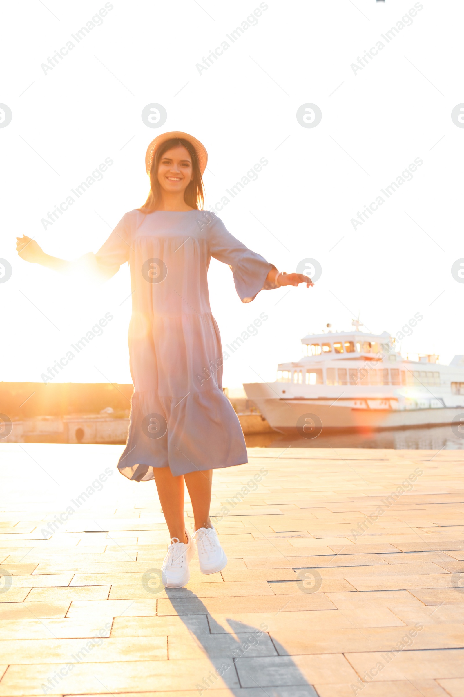 Photo of Young woman walking on pier at sunset light