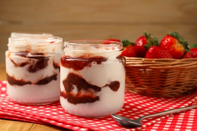 Photo of Tasty yoghurt with jam and strawberries on wooden table, closeup