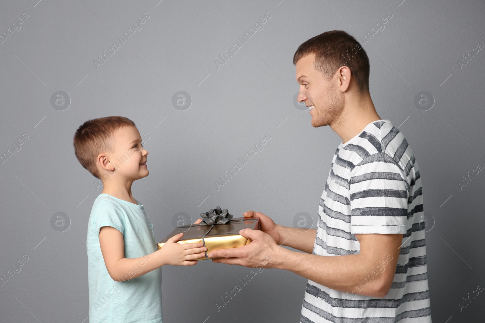 Photo of Man receiving gift for Father's Day from his son on grey background