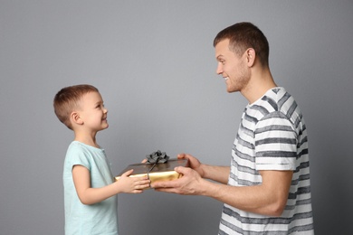 Photo of Man receiving gift for Father's Day from his son on grey background